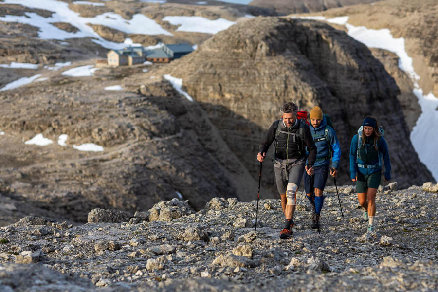 Felsenlandschaft in den Dolomiten, im Vordergrund eine Wandergruppe mit Wander Bandage und Wander Socken, im Hintergrund ein Wanderhütte