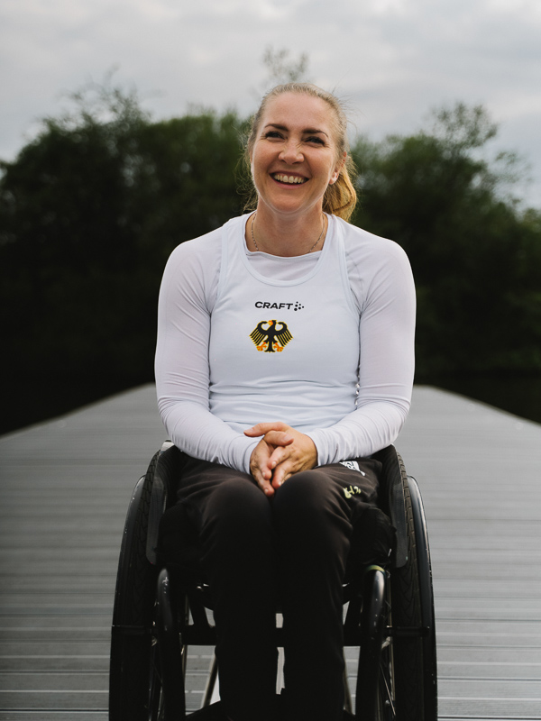 Die deutsche Sportlerin Edina Müller sitzt im Rollstuhl auf einem Steg und lacht in die Kamera.