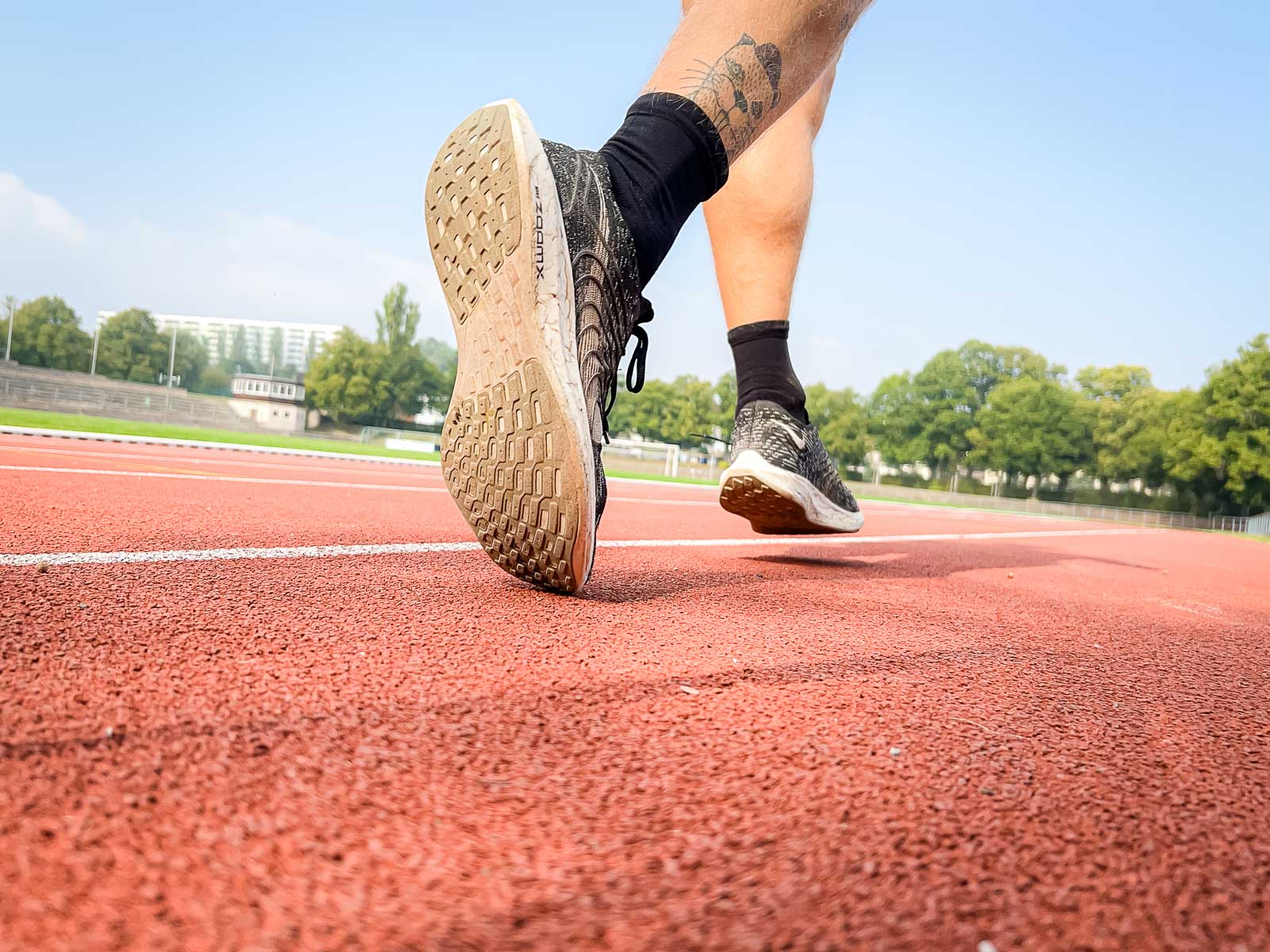 Nahaufnahme der Schuhe eines Läufers auf der roten Laufbahn, während er für das Training bereit ist. Die Szene symbolisiert Entschlossenheit und sportliche Zielstrebigkeit.