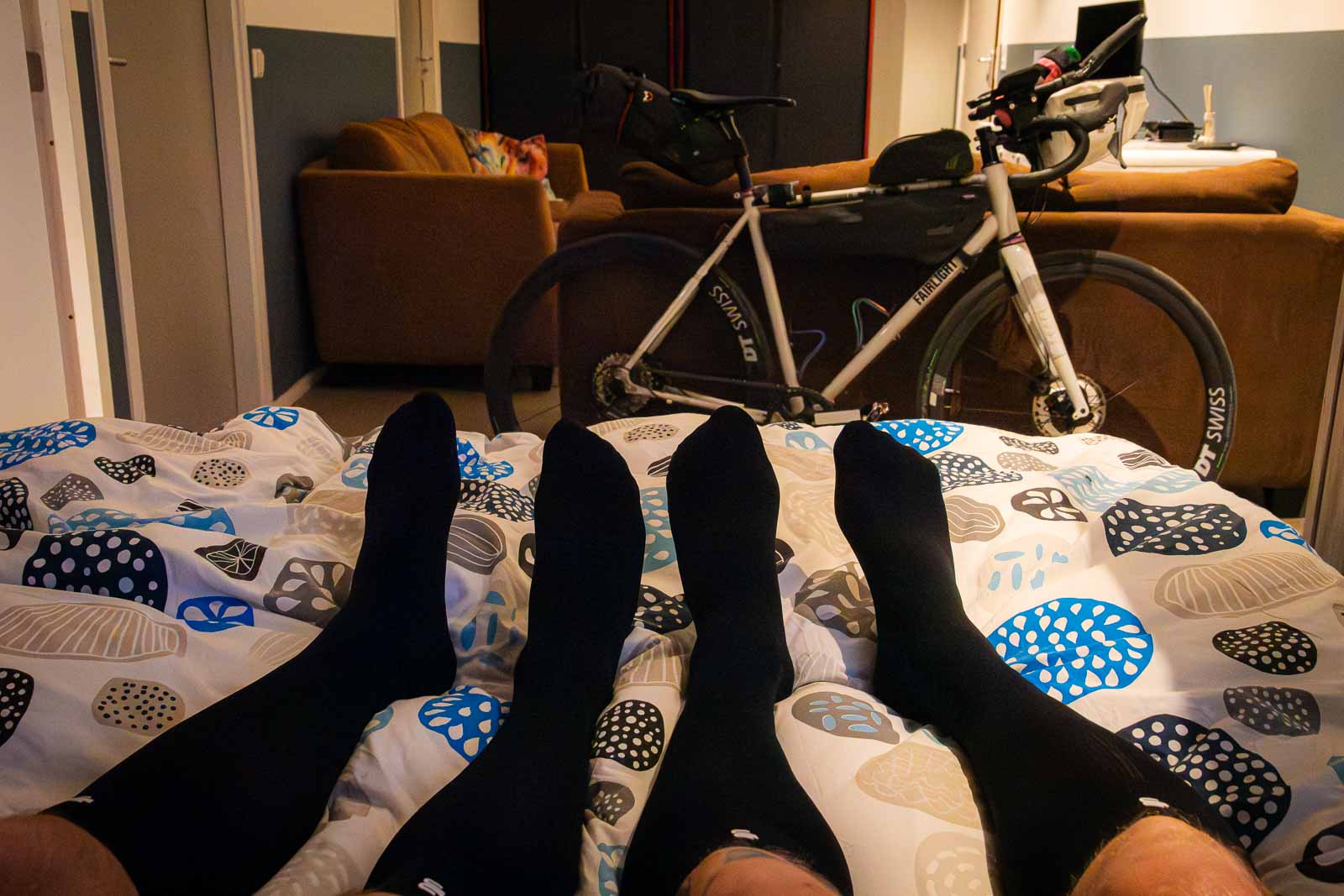 Zwei Teilnehmer des Race around the Netherlands liegen nach einem anstrengenden Tag im Bett und tragen Recovery Socken.
