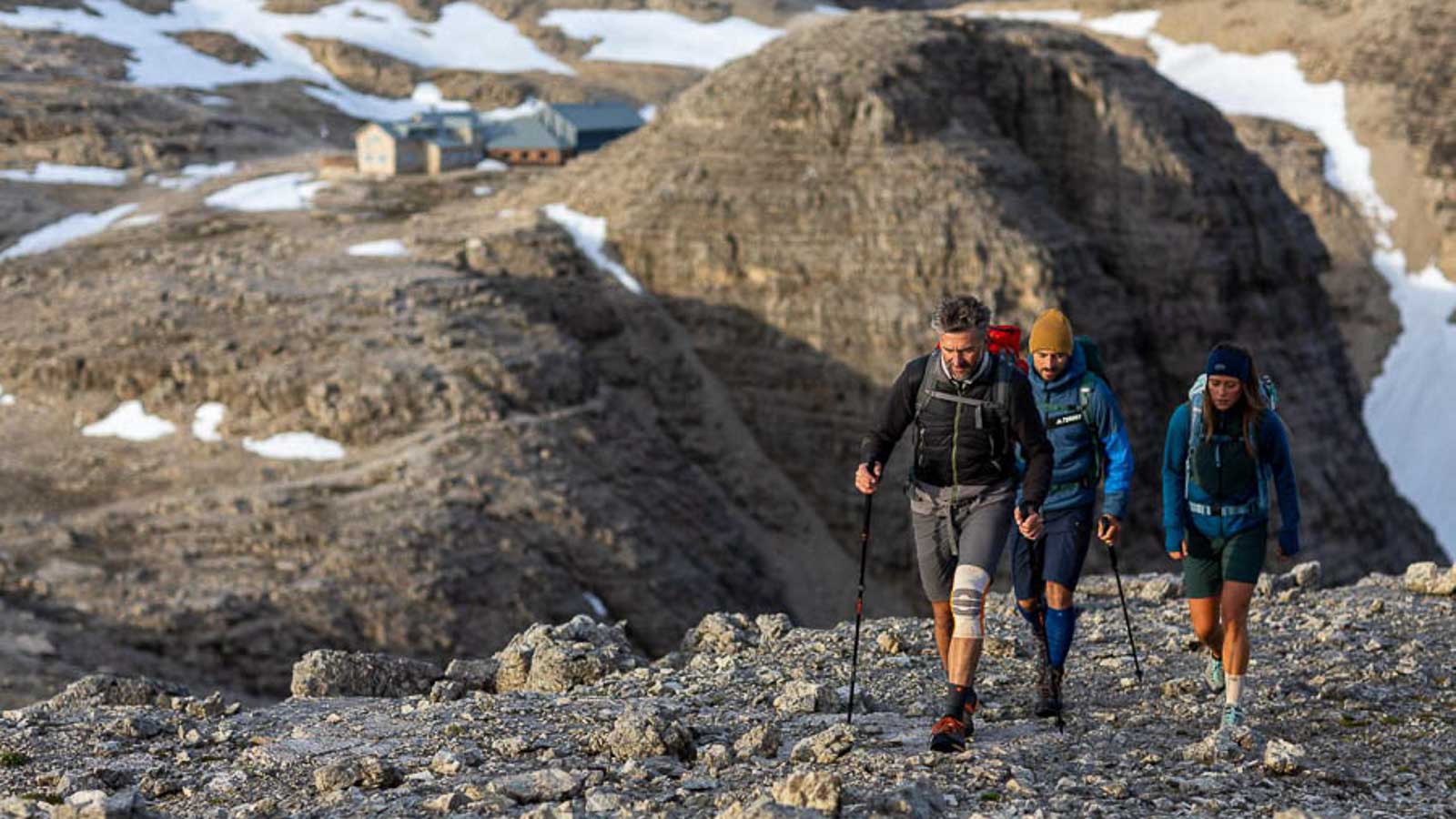 Felsenlandschaft in den Dolomiten, im Vordergrund eine Wandergruppe mit Wander Bandage und Wander Socken, im Hintergrund ein Wanderhütte