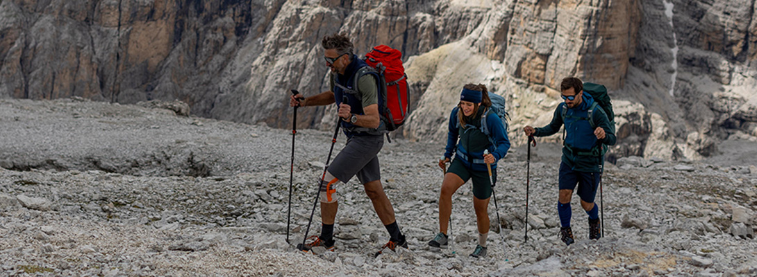 Drei Bergsteiger beim Wandern zwischen steinigem Geröll, der erste trägt eine Wander Kniebandage