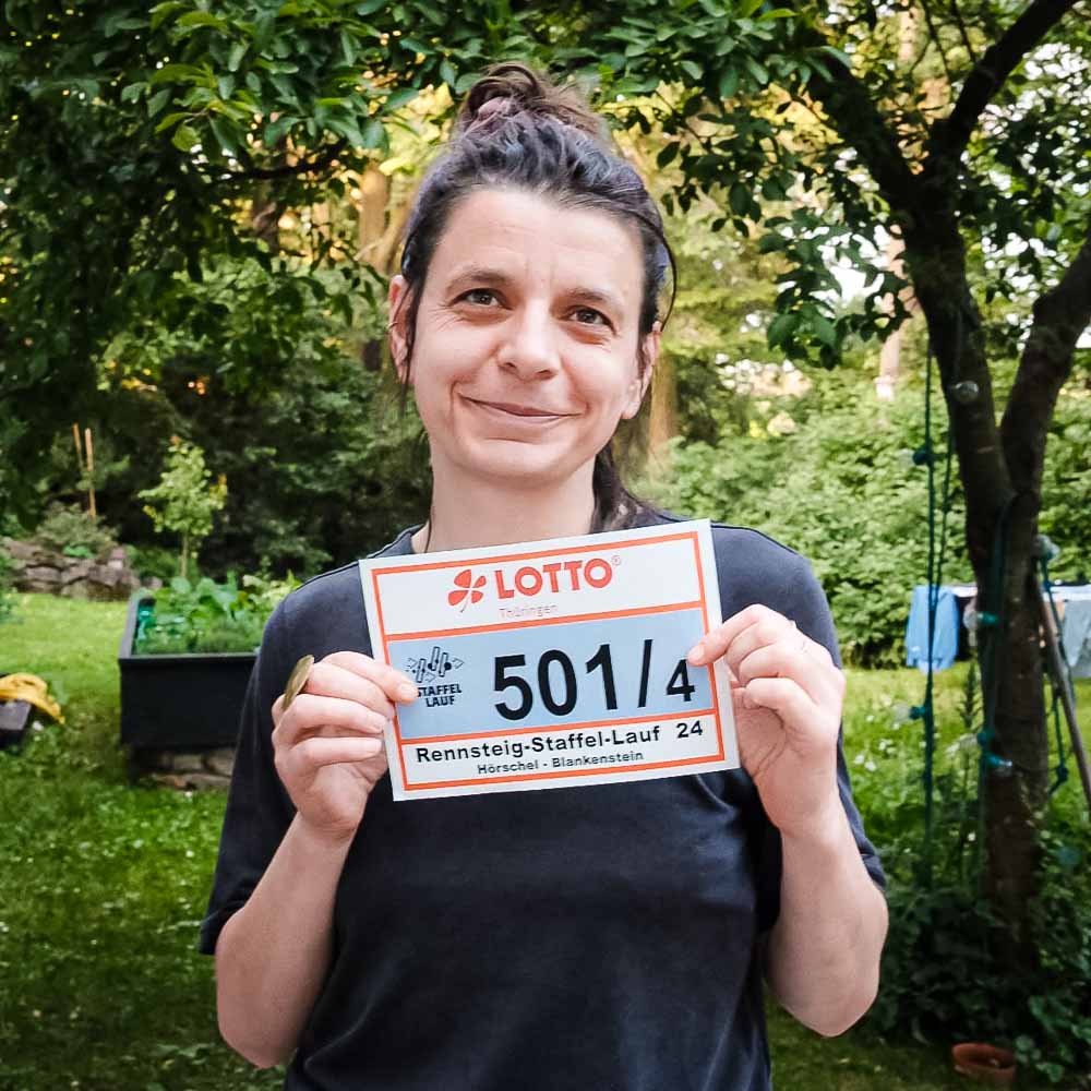 Frau hält lächelnd ihr Startnummernschild in der Hand