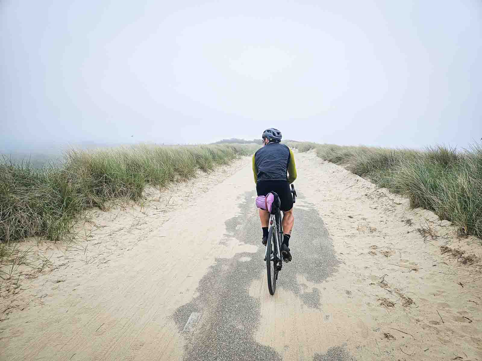 Ein Radfahrer fährt über schönen Dünenstraße die teilweise mit Sand bedeckt ist.