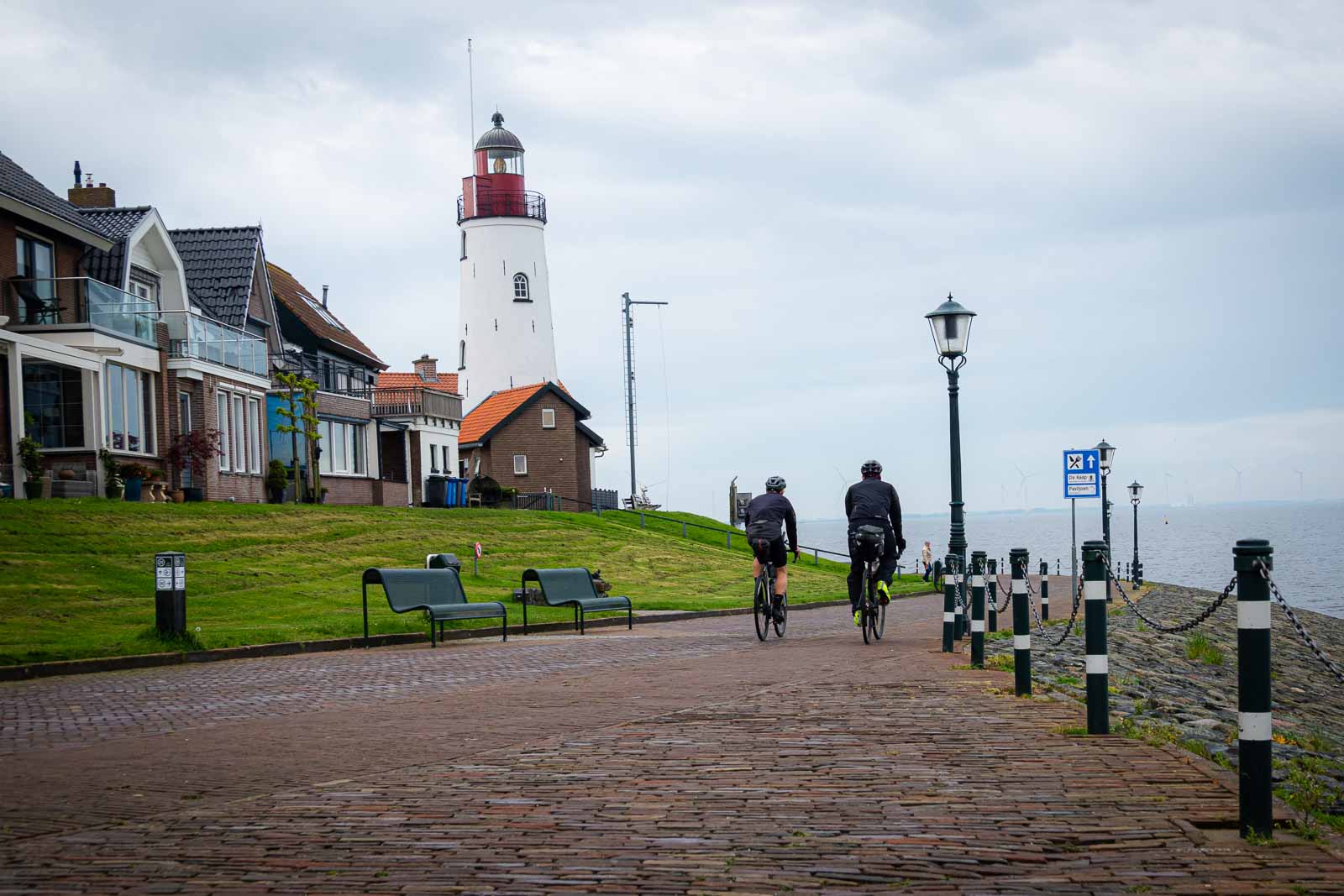 Zwei Ultra-Cycling Radfahrer von hinten die eine Promenade entlang fahren wo ein Leuchtturm steht.